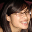 Pixelated close-up of a person with dark hair, light skin tone, and visible ear; mouth is open in a smile showing teeth.