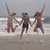 Three figures in swimwear jump on a beach with arms raised, holding hands against a gray sky and water background.