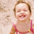 A child in a pink and yellow swimsuit smiles broadly on a sandy beach background.