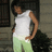 Pixelated figure in white tank top and light green pants stands with arms at sides against dark and light gray background.