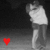 A grayscale figure with a white top and dark lower body stands against a dark background, with a small red heart symbol in the bottom-left corner.