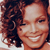 A pixelated close-up of a person with curly brown hair smiling broadly, showing teeth, against a dark background.