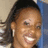 A pixelated close-up of a person with dark hair tied back, smiling broadly against a blurred background.
