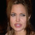 Pixelated close-up of a person with light brown hair, fair skin, and visible mouth and eye details against a dark background.