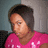 Pixelated image of a person with short dark hair wearing a pink shirt with white patterns, set against a blurred background.