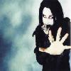 Static 100x100 pixel icon showing a person with long black hair in dark clothing holding up a hand against a blurred blue-gray background.