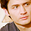 Static pixelated close-up of a person's face with brown hair and light skin, wearing dark clothing against a plain background.