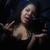A person with long dark hair in a black top makes hand gestures against a dark background, captured across three showing slight movement
