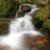 A pixelated static image shows a white waterfall flowing downward between green foliage and brown rocky terrain.