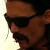 Pixelated close-up of a person's face wearing dark sunglasses and a brown cap, with a light background on the left side.