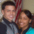 Two people pose together in front of an American flag, with the right person's face blurred and a gray background on one side.