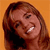 Static pixelated image of a person with long brown hair against an orange background, showing partial facial features and a smiling expression.