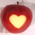 A red apple with a brown stem and a glowing heart-shaped cutout in the center, set against a light background.