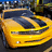 Yellow car with black racing stripes on hood, front view, static image with no visible motion.