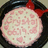 A circular pink and white patterned icon with a red bow on top, set against a dark background.