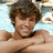 Pixelated image of a person with curly brown hair, light skin tone, and dark clothing against a blue background.