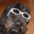 Pixelated image of a dark-furred animal wearing white sunglasses, with cyan text 'MAGGIE' and '=]' on the right side.