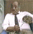 A man in a white shirt and dark tie stands with arms crossed, transitioning from a neutral expression to a smile