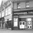 Black-and-white pixelated image of a building facade with multiple rectangular windows and a central door, showing architectural details and a street-level view.