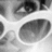 A grayscale pixelated image of a stylized face with large oval eyes and a smooth curved nose, set against a light background with darker abstract shapes.