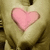 A pair of hands forms a heart shape with fingers, holding a pink heart-shaped object against a beige background.
