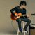 A person in dark clothing plays an orange electric guitar while seated on a stool, with pink text reading "Kevin Jonas" and "My Guitar Hero" displayed nearby.