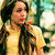 A pixelated static image shows a person with long dark hair wearing a yellow top, holding an object near their face against a blurred green and white background.