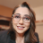 Pixelated portrait of a person with long brown hair, light skin, and glasses, wearing a dark top against a blurred background.