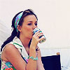 A woman with a colorful headband drinks from a patterned cup while wearing a white towel over her shoulder.
