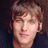A pixelated image of a person with light brown hair and blue eyes, alongside pixelated text reading 'may i suggest a...' and 'cappi-ccino?' on black and gray backgrounds.