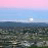 Pixelated static image of a sunset over water with layered sky colors and a bright sun or moon near the horizon.