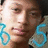 Pixelated close-up of a person's face with light skin tone, brown eyes, and dark hair; blue circular patterns on left and right edges.