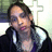 Pixelated image of a person with dark hair wearing a black jacket over a light shirt, holding an object near their face against a blurred background.