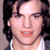 Static pixelated image of a person's face with dark hair and light skin, wearing a white top against a neutral background.