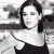 Black-and-white photo of a person with dark shoulder-length hair wearing a sleeveless top, positioned next to green background with pixelated text.