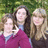 Three people stand outdoors with green foliage background; pixelated text elements appear in bright green on black space below and right of the photo.