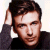 Static pixelated image of a person with dark hair wearing a black top, hand raised near head against light background.