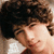 Pixelated close-up of a person with dark curly hair, light skin tone, and visible facial features including eyes, nose, mouth, and ear.