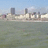 Cityscape view across water with buildings under blue sky, showing subtle animation changes in cloud positions and water texture.