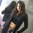 A pixelated static image shows a person with long dark hair wearing a black top, holding an object near their waist against a light background.