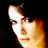 Pixelated close-up of a person's face with warm-toned skin, dark eyes, and a neutral expression against a black background.