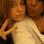 Two people in a close-up pose with one person making a hand gesture, set against a brown background.