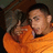 A pixelated image of a person in an orange shirt making a hand gesture with fingers extended, set against a dark background.