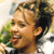 Pixelated close-up of a person's face with light brown hair, smiling mouth showing teeth, green foliage background.