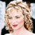 Pixelated close-up of a person with curly light brown hair, red lips, and a black garment against a light blue and white background.