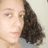 Pixelated close-up of a person with light skin tone, dark brown curly hair, and visible eyes and lips against a pale background.