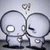 Two stylized figures with large circular heads and simple bodies stand side-by-side against a light gray background, one with a white eye and the other with a black eye.