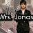A woman in a black suit with arms crossed appears against a metallic background, with text reading "Mrs. Jonas" visible on the left side.