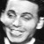 Black-and-white pixelated portrait of a smiling person with short hair, wearing a light-colored collared shirt against a dark background.