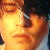 Pixelated close-up of a face with warm orange and yellow tones, showing partial features including an eye, nose, and mouth against a dark background.
